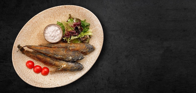 Fried goby fish in a plate on a dark concrete background