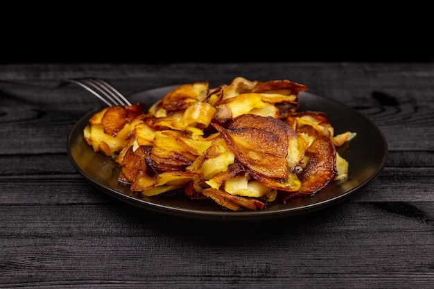 Photo fried homemade potato chips in a black plate on a wooden rustic background.