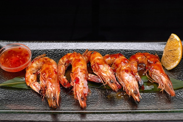 Fried king prawns on a bamboo leaf, on a transparent plate, with lemon and sauce