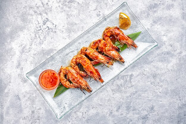 fried king prawns on a bamboo leaf, on a transparent plate, with lemon and sauce