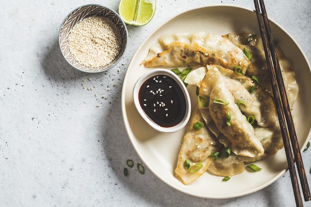 Fried Korean dumplings with green onion and sauce on white plate, top view.