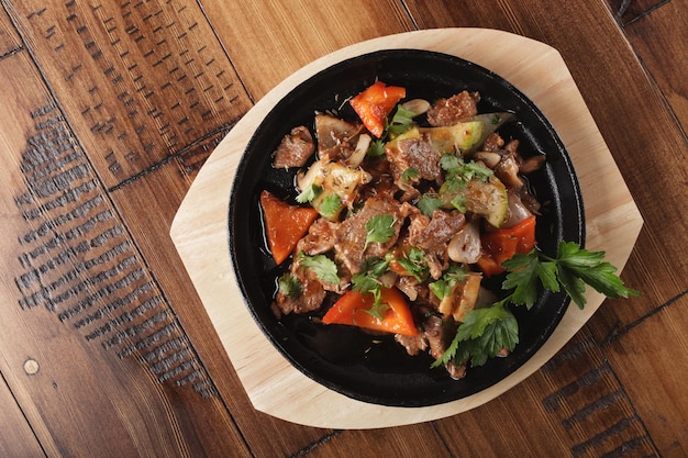 Fried lamb meat slices with vegetables in a pan. Wooden background