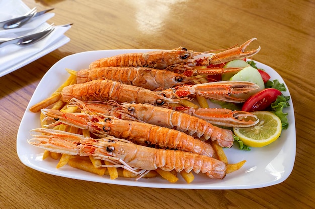 Fried langoustines with french fries and lemon on the table at sunny day