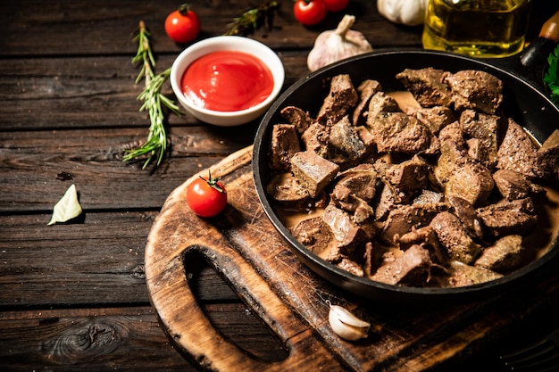 Fried liver in a frying pan on a cutting board with tomato sauce