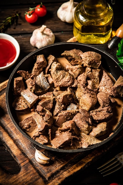 Fried liver in a frying pan on a cutting board with tomato sauce