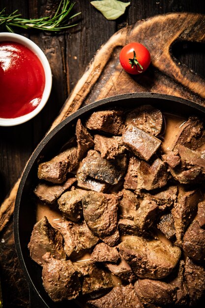 Fried liver in a frying pan on a cutting board with tomato sauce