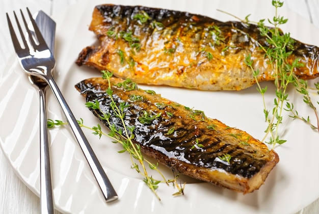 Fried mackerel fillets with spices and thyme on a white plate closeup