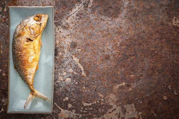 Fried mackerel in rectangular ceramic plate on rusty texture background with copy space for text, top view