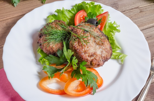 Fried meat cutlets with vegetables and herbs on a white plate close-up