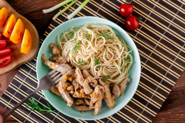 Fried meat and spaghetti on a plate on a wooden background with tomatoes and herbs.