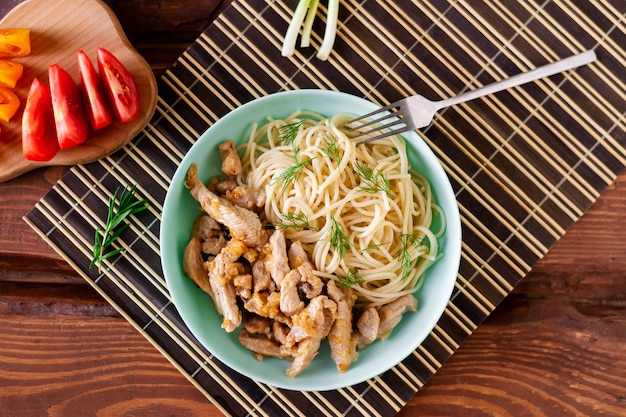 Fried meat and spaghetti on a plate on a wooden background with tomatoes and herbs.