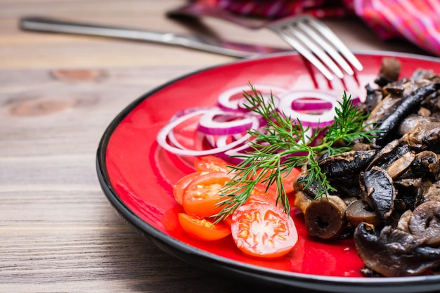 Fried mushrooms, onion and cherry tomatoes on a plate on a wooden table