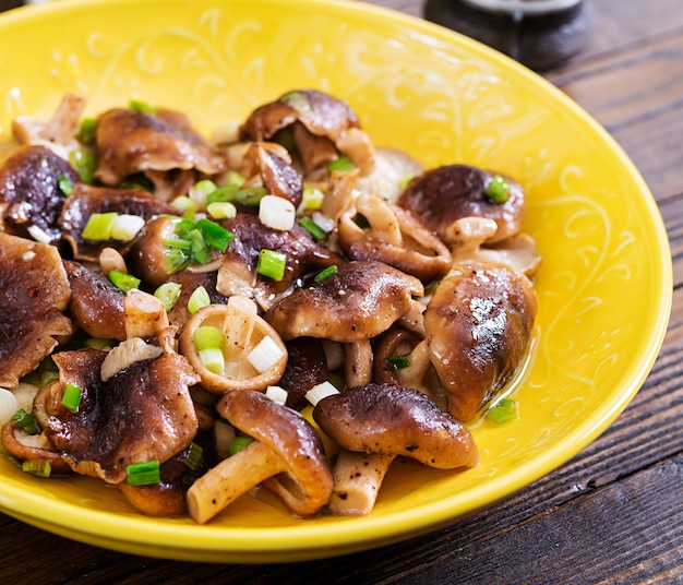 Fried mushrooms shiitake with green onion on wooden table. Chinese food.
