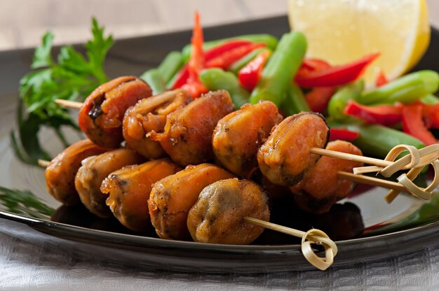 Fried mussels with onions on skewers c garnish of green beans and paprika