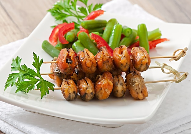 Photo fried mussels with onions on skewers c garnish of green beans and paprika