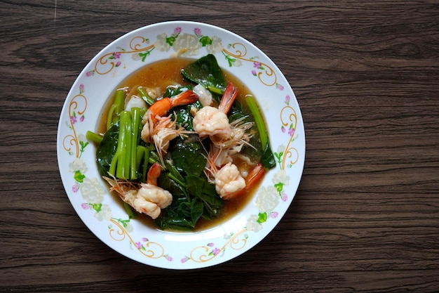 Fried noodle with shrimps and kale soaked in gravy on wooden table