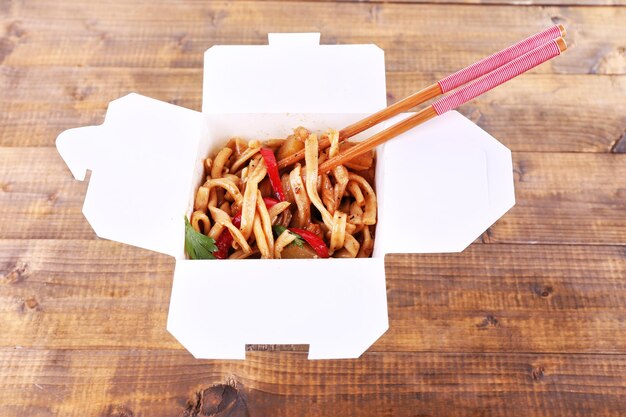 Photo fried noodles and sticks in takeaway box on wooden background