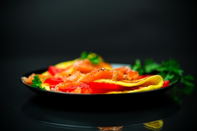 Fried omelet with tomatoes vegetables and pieces of lightly salted red fish isolated on a black background