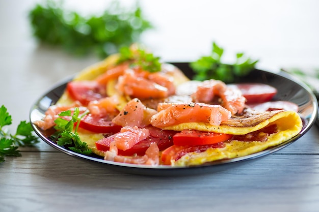 Fried omelette with tomatoes vegetables and pieces of lightly salted red fish on a wooden