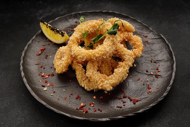 Fried onion rings in batter with spices on a black plate on a black background