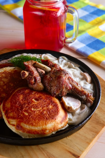 Fried in oven ribs with fritters and onion sauce. Cast iron pan on wooden cutting board and glass with cranberry juice