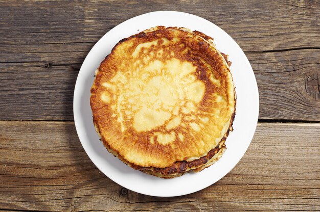 Fried pancakes in plate on rustic wooden table, top view