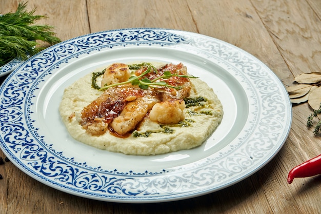 Fried perch fillet with mashed cauliflower in a white plate on a wooden surface. Delicious seafood with garnish