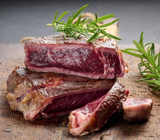 Fried piece of beef ribeye, cut into pieces on a brown wooden board, rare doneness