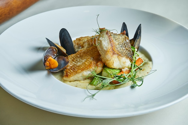 Fried pike perch fillet with cream sauce and mussels in a white bowl. Restaurant serving dishes. Seafood for lunch