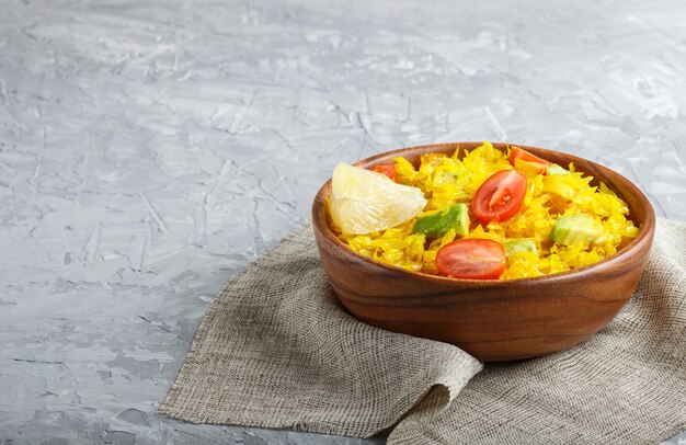 Fried pomelo with tomatoes and avocado in wooden plate on gray concrete background.