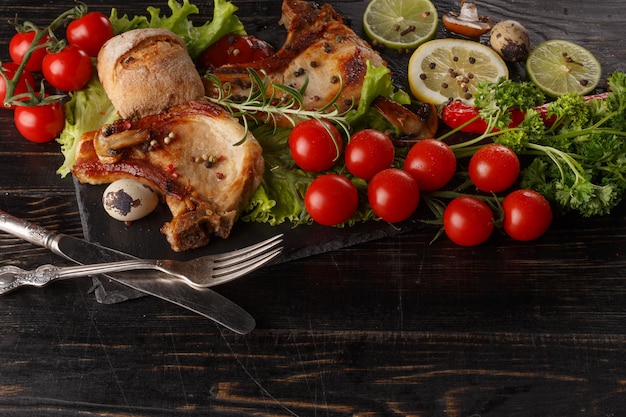 Fried pork chop on a black plate with spices, herbs and tomatoes.