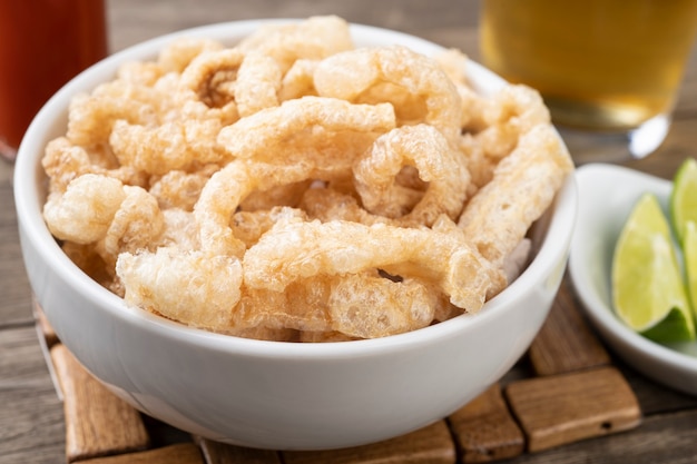 Fried pork cracklings on a white bowl with lemon and beer over wooden table.