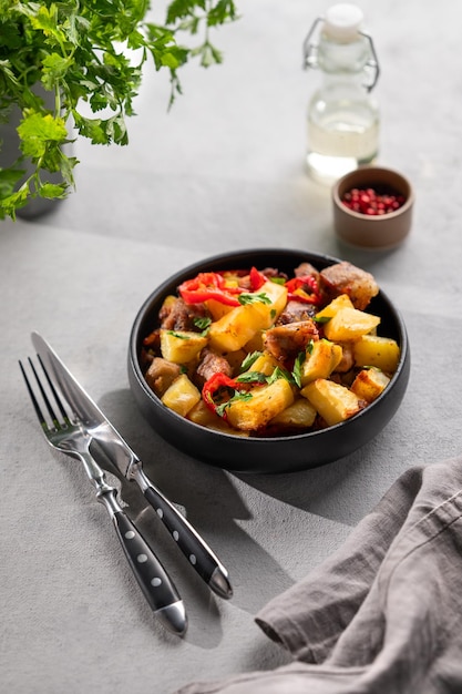 Fried pork meat with potatoes onions and peppers National homemade Georgian dish ojakhuri in a black bowl on a light background