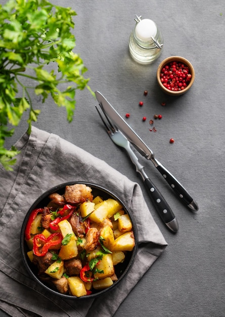 Photo fried pork meat with potatoes onions and peppers national homemade georgian dish ojakhuri in a black frying pan on a dark background with spices and fresh herb