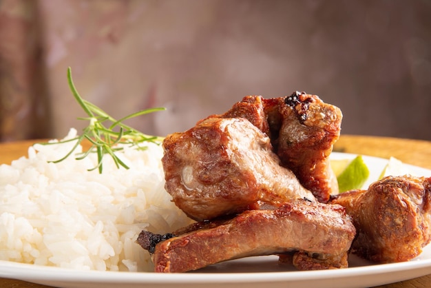 Fried pork ribs, rice and condiments on a white plate arranged on light rustic wood, selective focus.