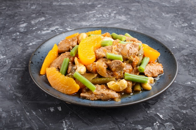 Fried pork with peaches, cashew and green beans on a black concrete background