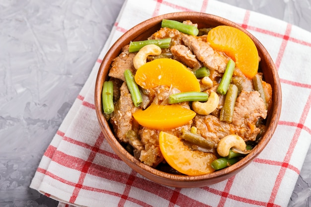 Fried pork with peaches, cashew and green beans in a wooden bowl on gray 