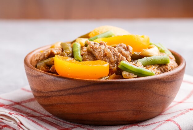 Fried pork with peaches, cashew and green beans in a wooden bowl on gray 