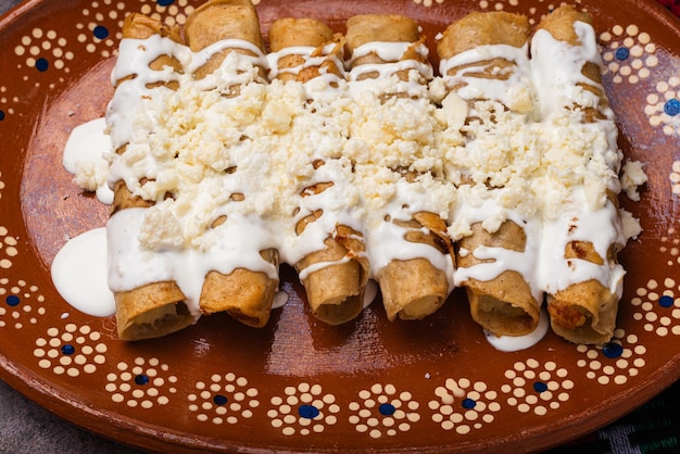 Жареные картофельные тако с сливками и сыром в мексиканском грязевом блюде Tacos dorados мексиканская еда