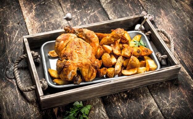 Fried potatoes with chicken on tray on wooden table.