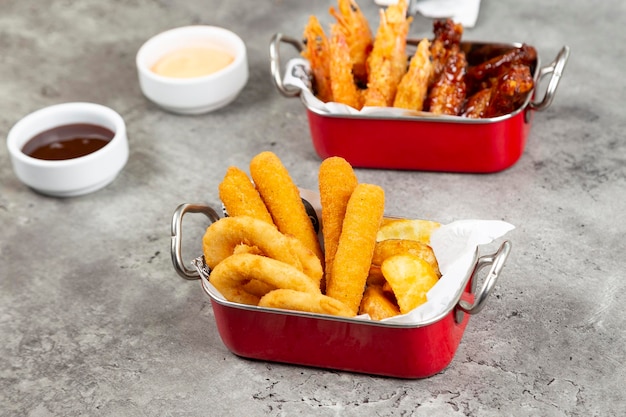 fried potatoes with fried chicken wings and shrimps in decorative metal plate in grey background