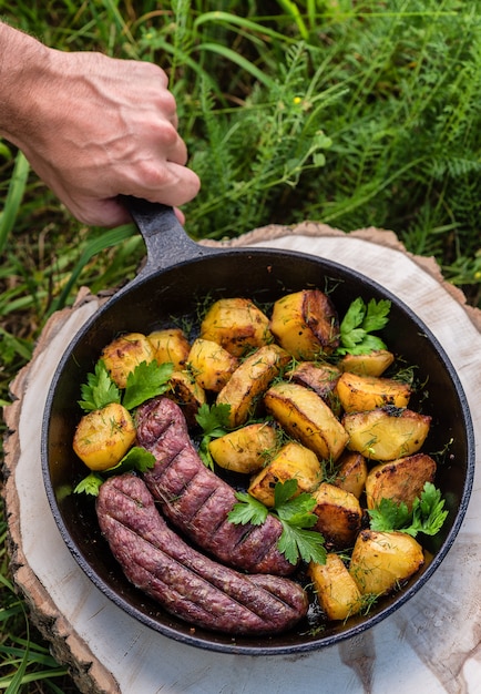 Fried potatoes with meat sausages in a cast-iron frying pan