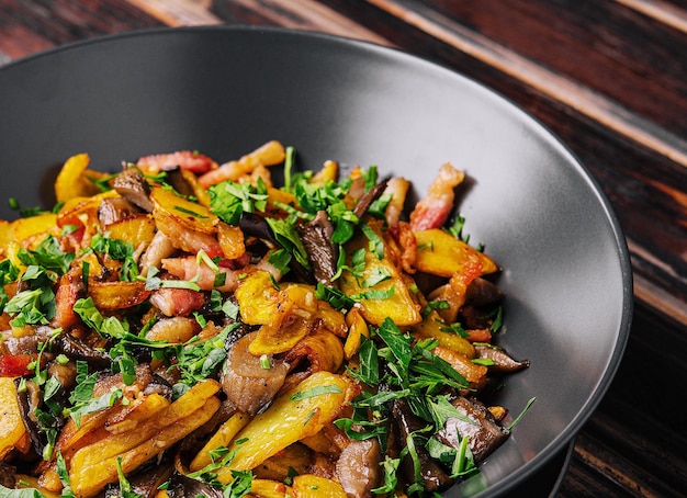 Fried potatoes with mushrooms on a black plate