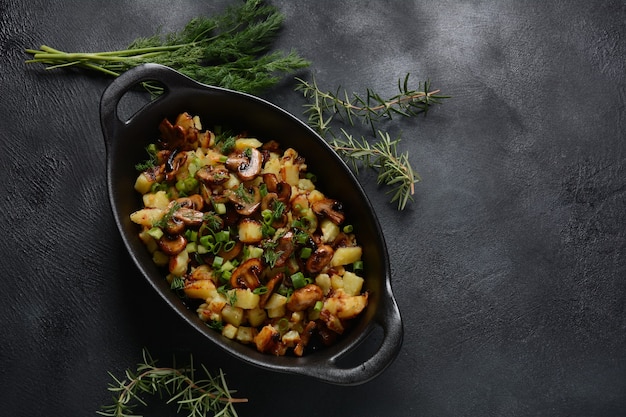 Fried potatoes with mushrooms in  frying bowl with herbs.