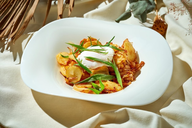 Patate fritte con un uovo in camicia in un piatto tovaglia bianca leggera dura