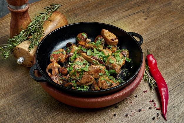 Patate fritte con carne di maiale, cipolle ed erbe in una padella decorativa su una superficie di legno. avvicinamento