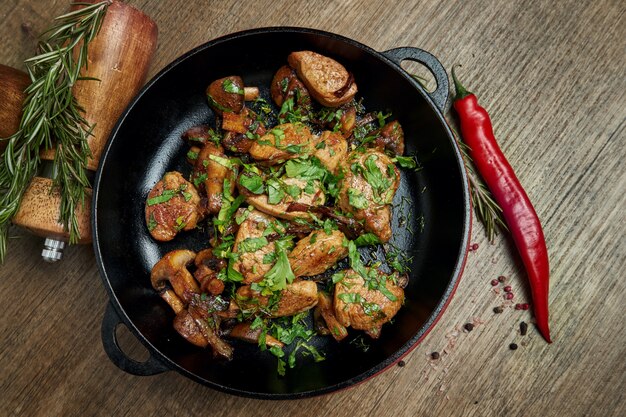 Patate fritte con carne di maiale, cipolle ed erbe in una padella decorativa su una superficie di legno. vista dall'alto su cibo gustoso.