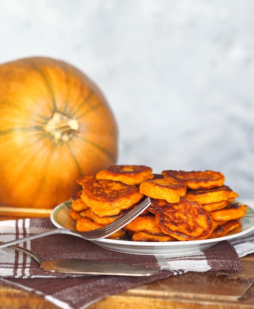 Fried pumpkin pancakes in a plate on the background of a large orange pumpkin