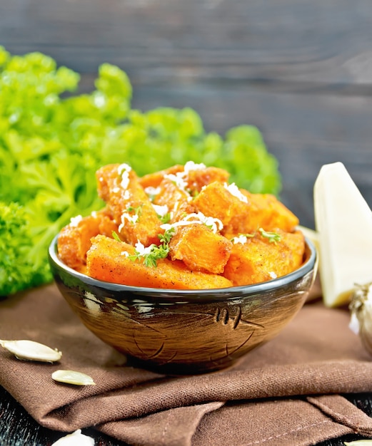 Fried pumpkin with spices and peppers, sprinkled with hard cheese in a bowl on a napkin, garlic, parmesan and parsley on wooden board background