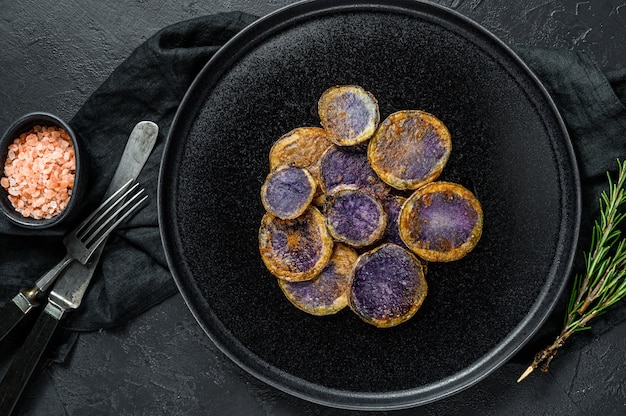 Fried purple potatoes with rosemary. Black background. Top view